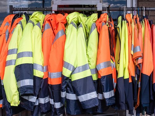 High-visibility safety jackets in bright yellow and orange hanging on a rack.